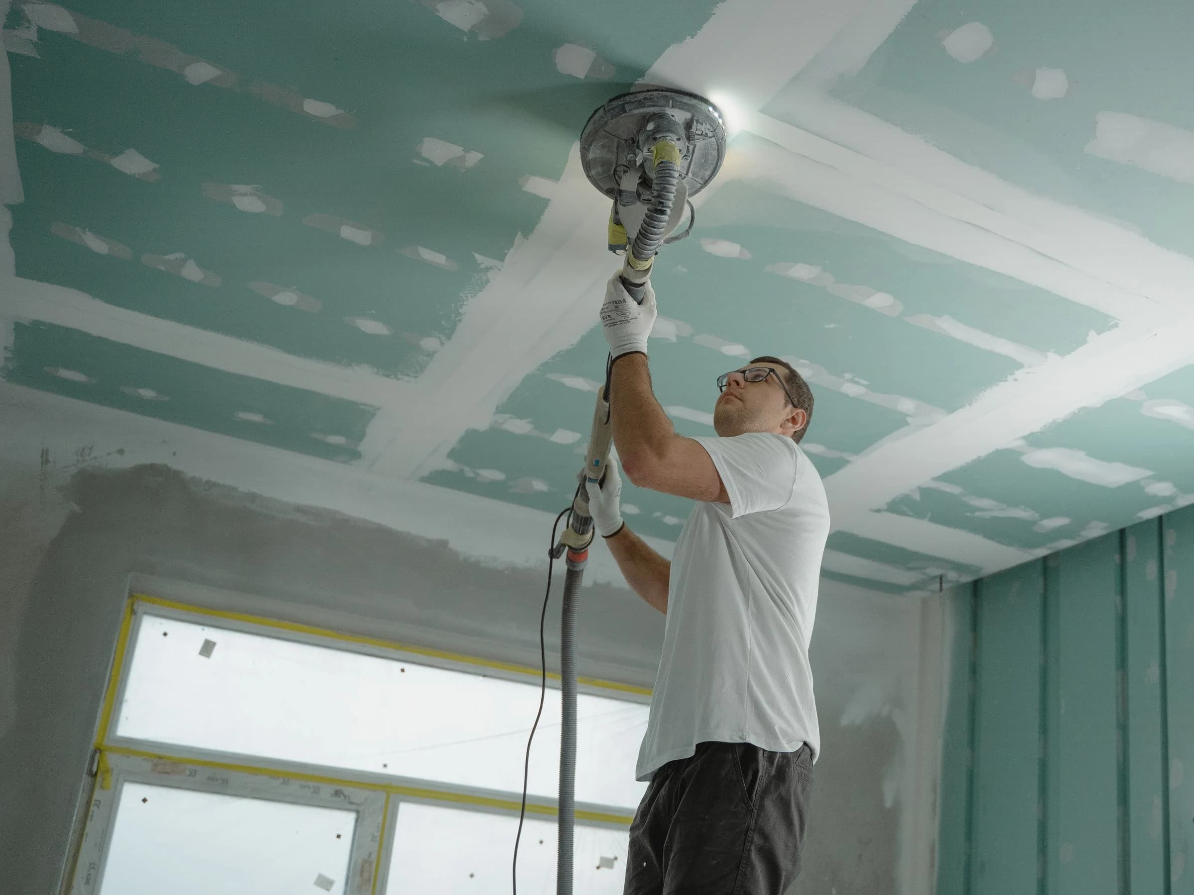 A worker sanding the joints of a gypsum-board ceiling during interior fit-out