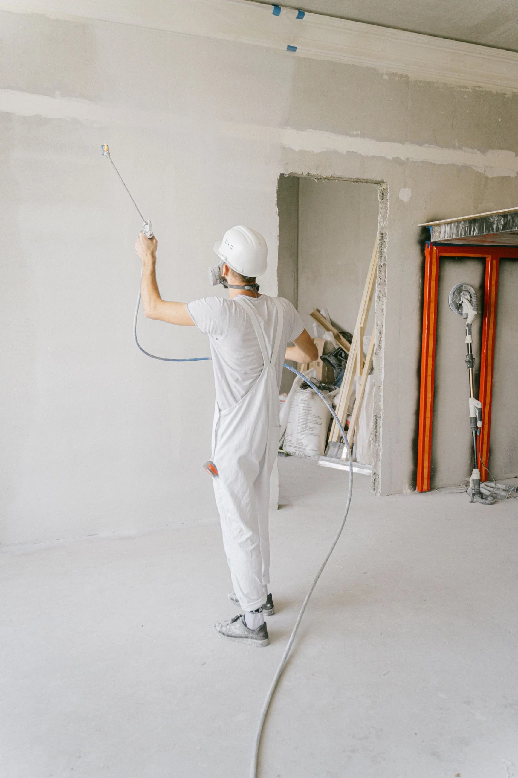 A worker applying primer to walls in an unfinished interior under renovation