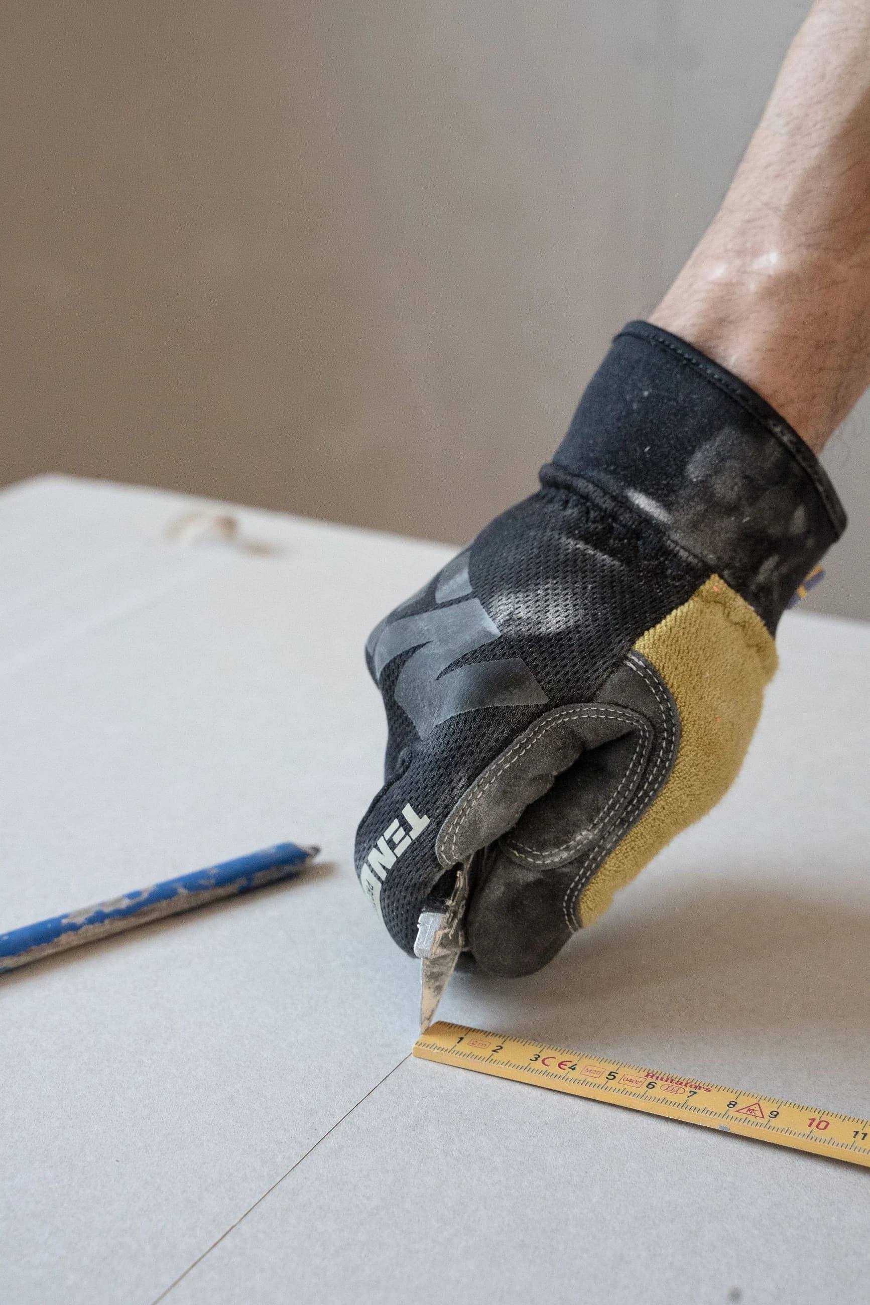 Gloved hands scoring plasterboard against a measuring rule before installation