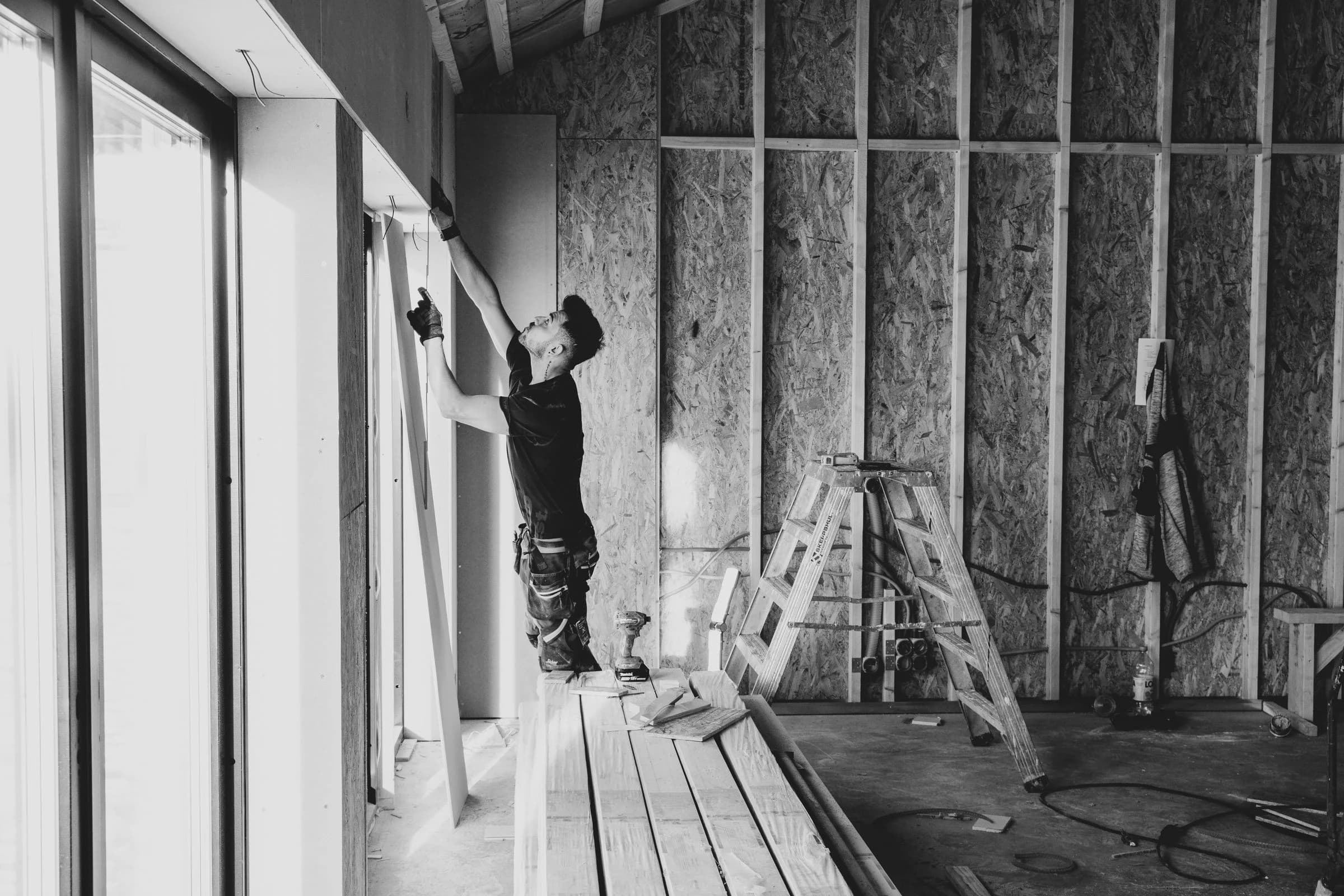 A worker fitting wall boards beside exposed timber framing during interior construction