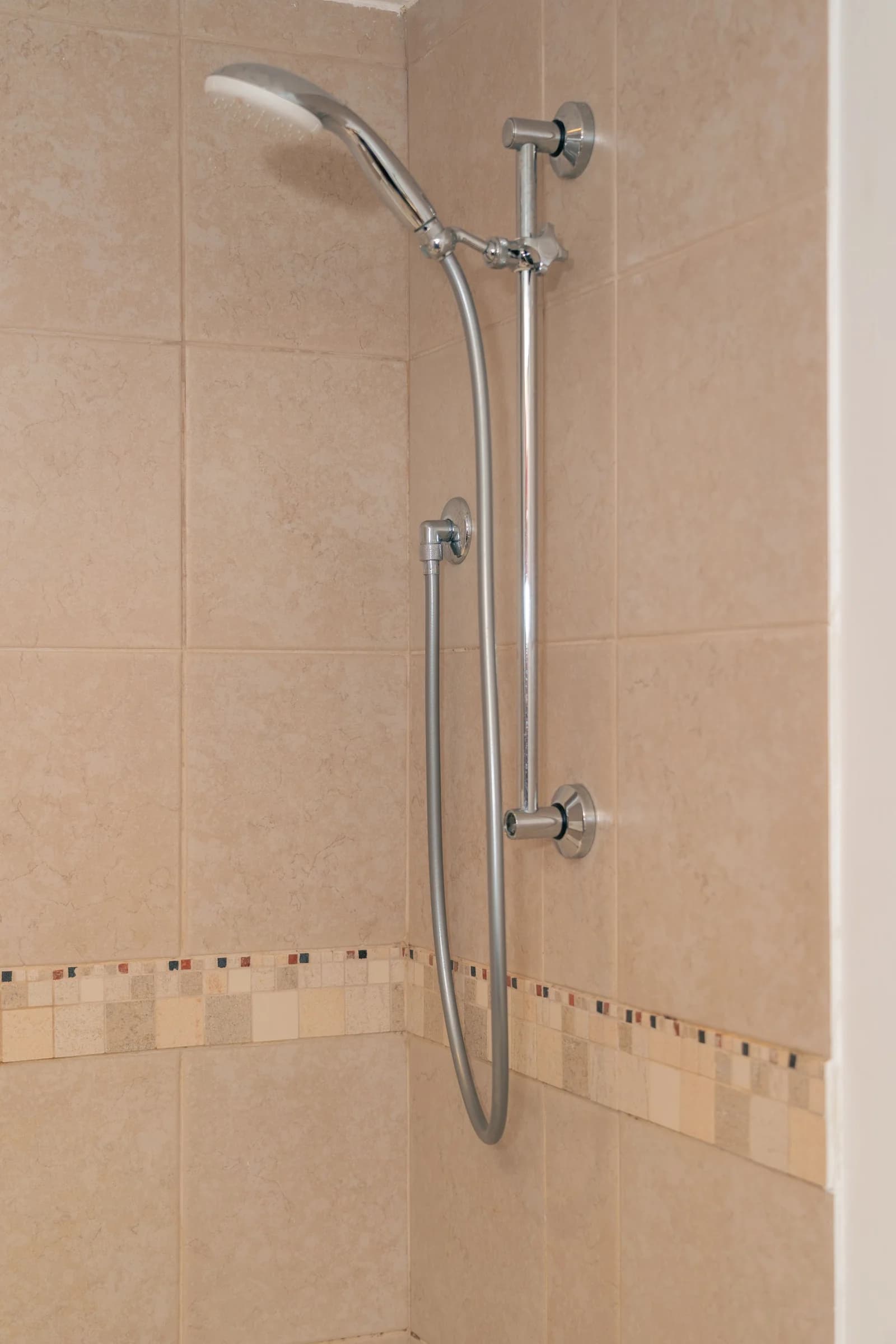 Chrome shower fixture and connected hose mounted on a tiled wall in Dubai